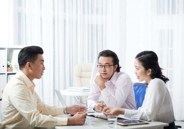 Young Asian men and woman sitting at table in modern office and coworking